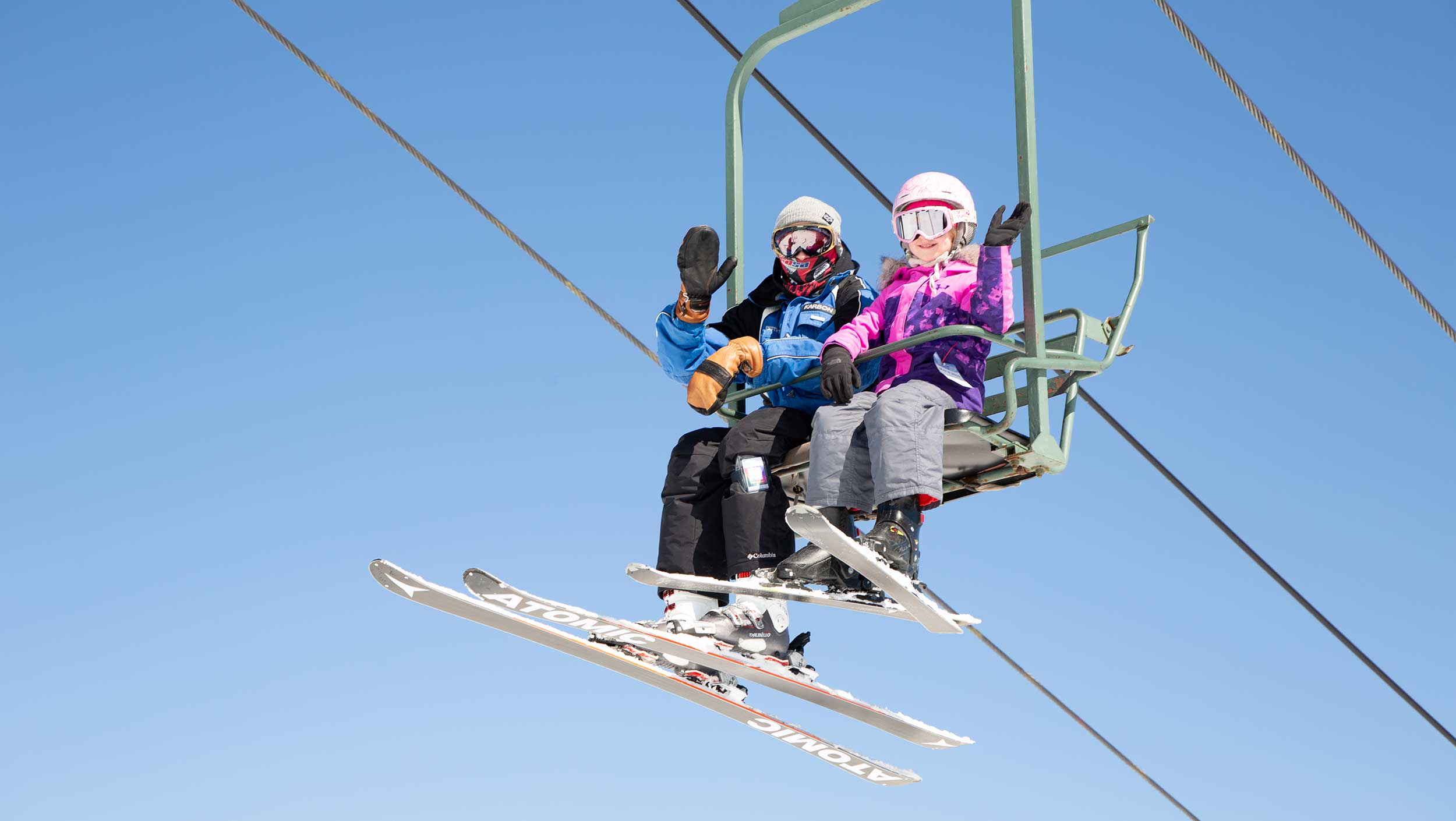 Two people wearing skis on a chair lift